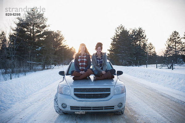 Zwei Frauen sitzen auf der Motorhaube im Schnee