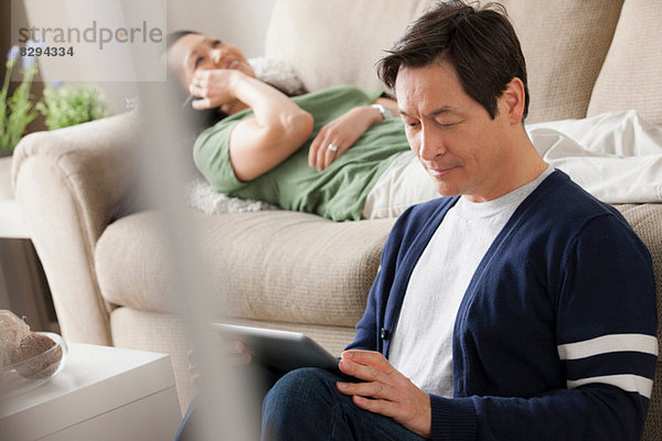 Reifer Mann mit digitalem Tablett  Frau auf dem Sofa liegend