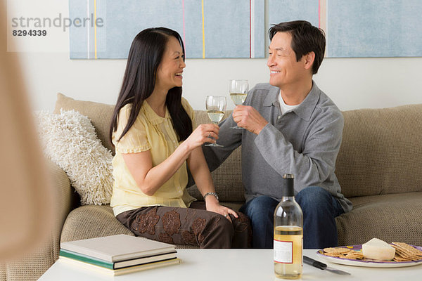 Reife Paare sitzen auf dem Sofa und rösten Weißwein.