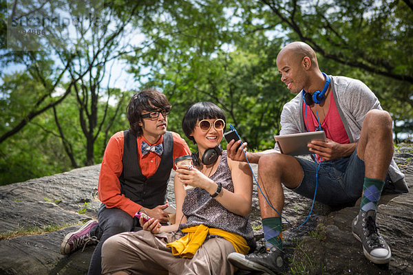 Drei Freunde sitzen auf Steinen mit mp3-Player und Tablett