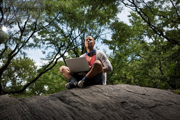 Junger Mann auf Felsen sitzend mit Laptop