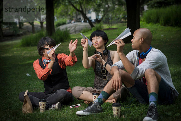 Drei Freunde mit Papierfliegern im Park