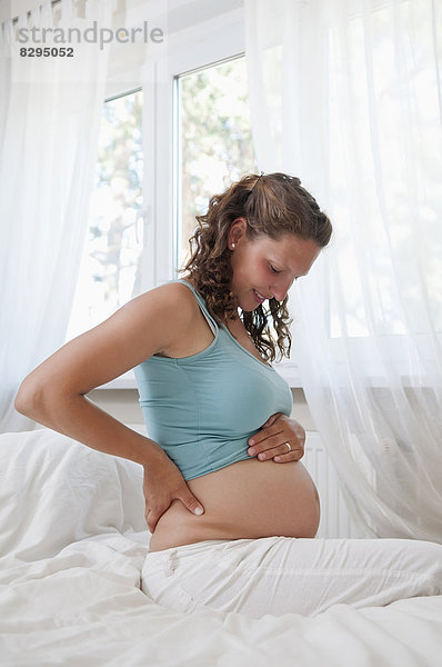 junge schwangere Frau auf dem Bett sitzend