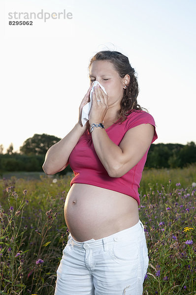 junge schwangere Frau mit Heuschnupfen auf einer Blumenwiese stehend