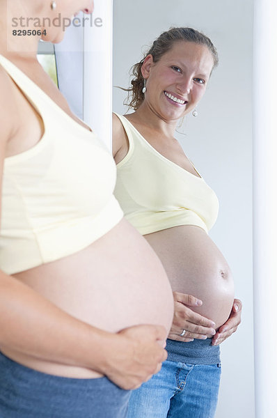 junge schwangere Frau schaut in den Spiegel