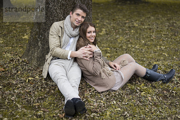 Glückliches Paar im Park am Baum sitzend