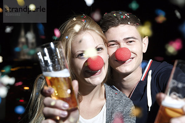 Germany  North Rhine Westphalia  Cologne  young couple with clowns noses toasting