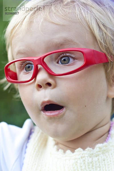 Porträt des erstaunten kleinen Mädchens mit roter Brille