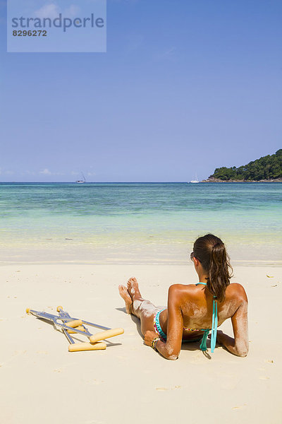 Thailand  Insel Koh Surin  Frau mit Krücken am weißen Sandstrand liegend