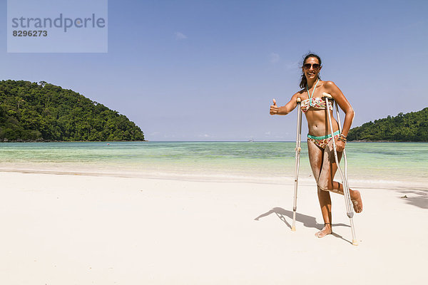 Thailand  Koh Surin island  woman with crutches standing at the white sandy beach