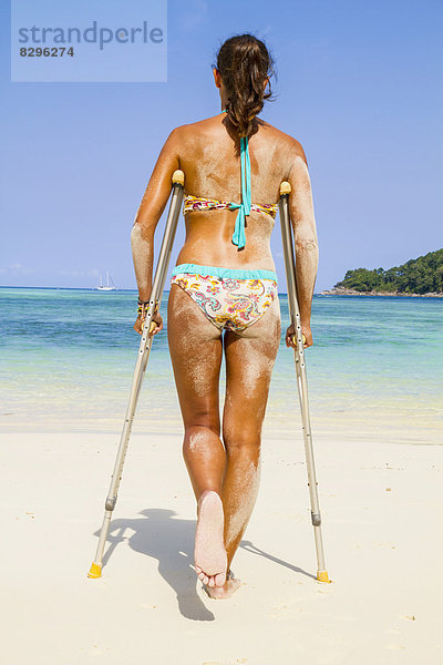 Thailand  Insel Koh Surin  Frau mit Krücken am weissen Sandstrand