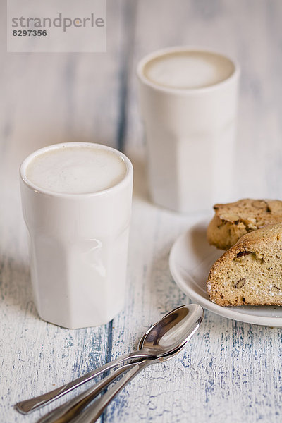 Cups of latte macchiatto with almond biscuits on wooden board