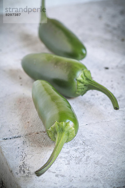 Drei grüne Jalapeno-Chilis (Capsicum annuum) auf weißem Schneidebrett  Studioaufnahme