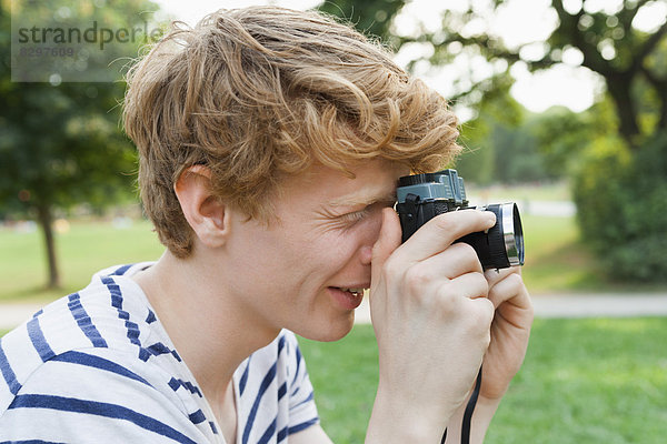 Junger Mann beim Fotografieren im Park mit einer altmodischen Kamera