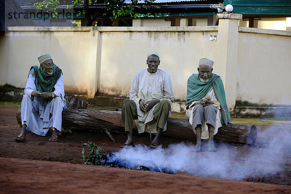 Drei Männer sitzen an einem Weg im Dorf Idool und beaufsichtigen ein Feuer