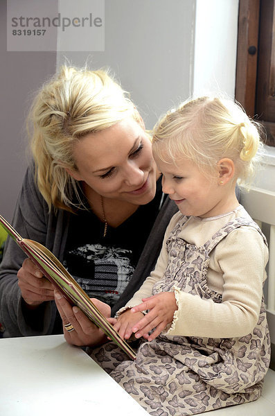 Mutter schaut mit ihrer kleinen Tochter ein Buch an