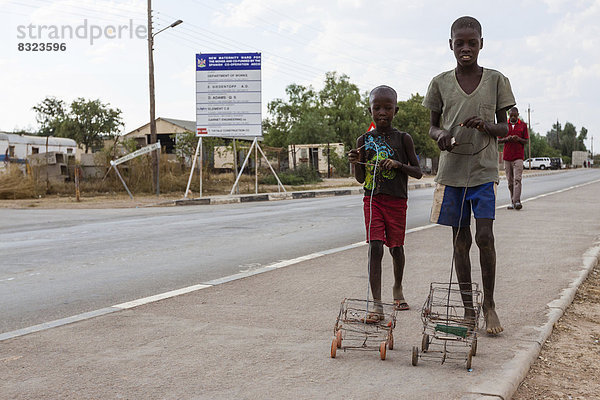 Zwei Himba-Jungen spielen mit ihren selbstgebauten Spielzeugautos am Straßenrand