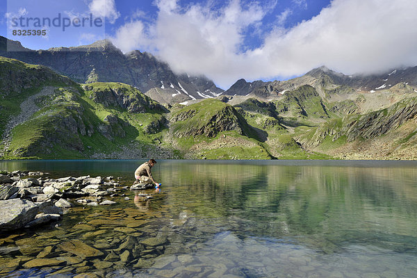 Bergsteigerin füllt Wasserflasche am Großen Schwarzsee oder Lago Nero  dahinter Schwarzwandspitze