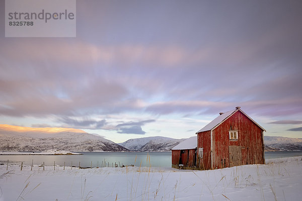 Rote Fischerhütte vor Fjord in winterlicher Landschaft