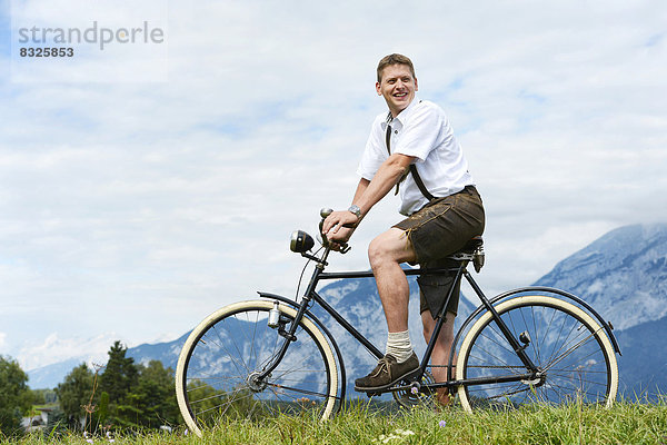 Mann mit Lederhose auf altem Fahrrad