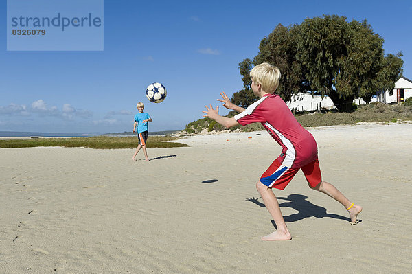 Jungen spielen Fußball am Strand