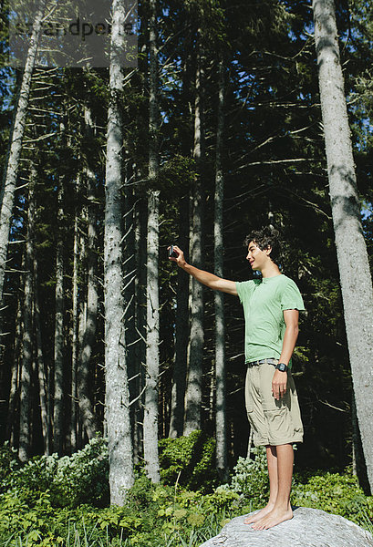 Ein Junge  der im Wald steht und ein Smartphone in der Hand hält  um ein Selbstporträt oder ein Foto zu machen  im Olympia-Nationalpark.