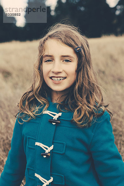 Ein junges neunjähriges Mädchen in einem blauen Seesackmantel  das in die Kamera lächelt.