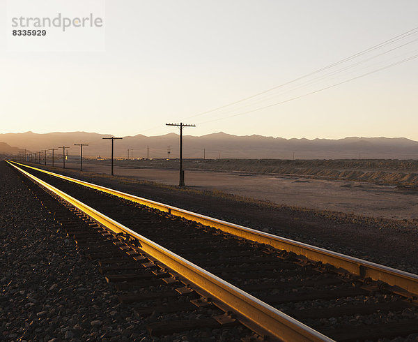 Eisenbahnschienen  die in der Abenddämmerung durch die flache Wüstenlandschaft Utahs führen.