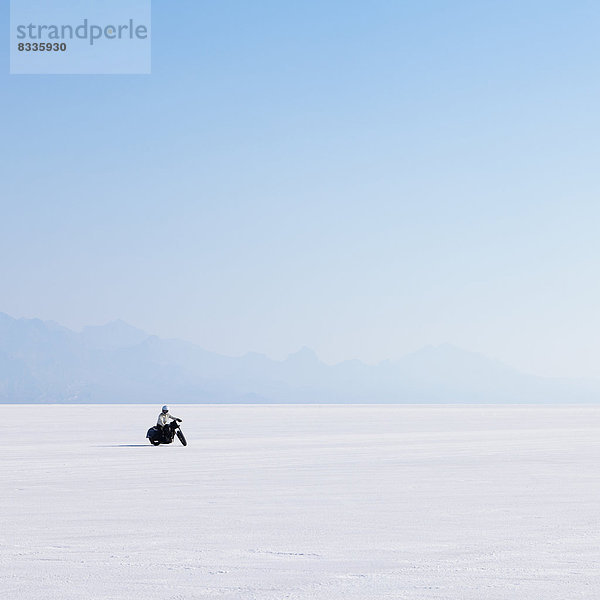 Motorradfahrer  der auf der flachen weißen Oberfläche der Salzpfanne auf den Bonneville Salt Flats fährt.