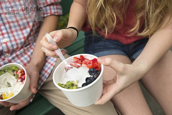 Junge Leute sitzen Seite an Seite und essen frisches Bio-Obst und Joghurt-Dessert.