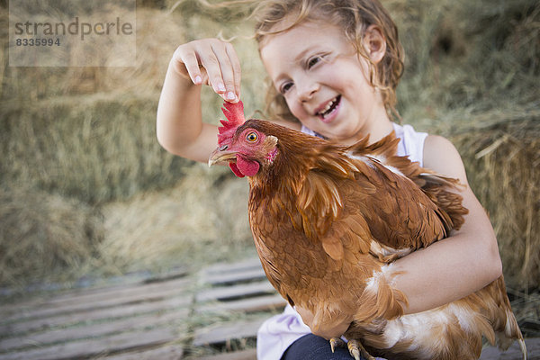 Ein junges Mädchen hält ein Huhn in einem Hühnerstall.