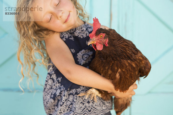 Ein junges Mädchen hält ein Huhn im Arm.