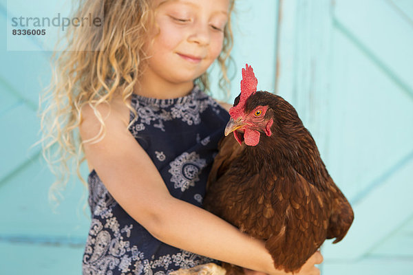 Ein junges Mädchen hält ein Huhn im Arm.