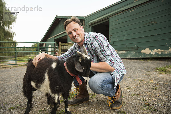 Ein Bio-Bauernhof in den Catskills. Ein Mann mit einer kleinen Ziege an einem Halfter.