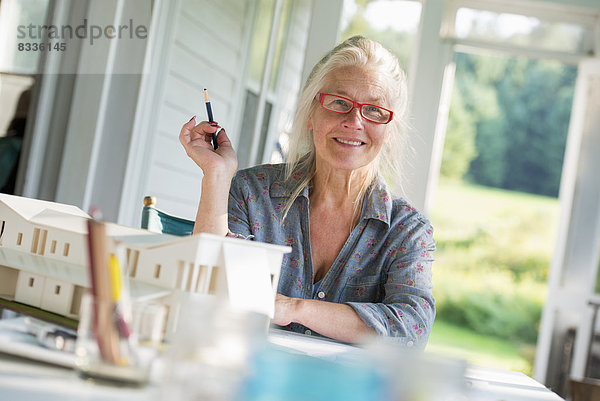 Eine Bauernhaus-Küche. Ein Modell eines Hauses auf dem Tisch. Ein Haus entwerfen. Eine Frau sitzt und hält einen Stift.