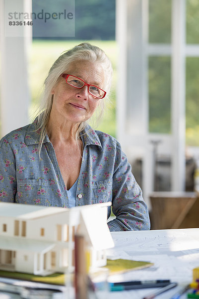 Eine Bauernhaus-Küche. Ein Modell eines Hauses auf dem Tisch. Ein Haus entwerfen. Eine Frau sitzt und hält einen Stift.