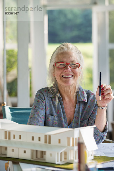 Eine Bauernhaus-Küche. Ein Modell eines Hauses auf dem Tisch. Ein Haus entwerfen. Eine Frau sitzt und hält einen Stift.