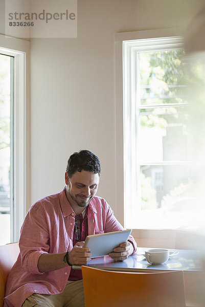Ein Mann sitzt an einem Café-Tisch und benutzt ein digitales Tablett.
