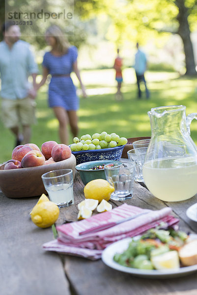 Ein sommerliches Buffet mit Obst und Gemüse  das auf einem Tisch aufgebaut ist. Menschen im Hintergrund.