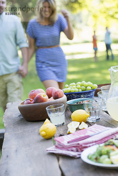 Ein sommerliches Buffet mit Obst und Gemüse  das auf einem Tisch aufgebaut ist. Menschen im Hintergrund.