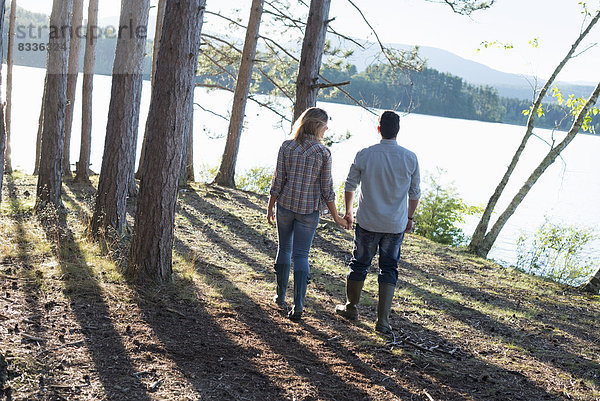 Ein Paar  das in einem Wald am Ufer eines Sees spazieren geht.