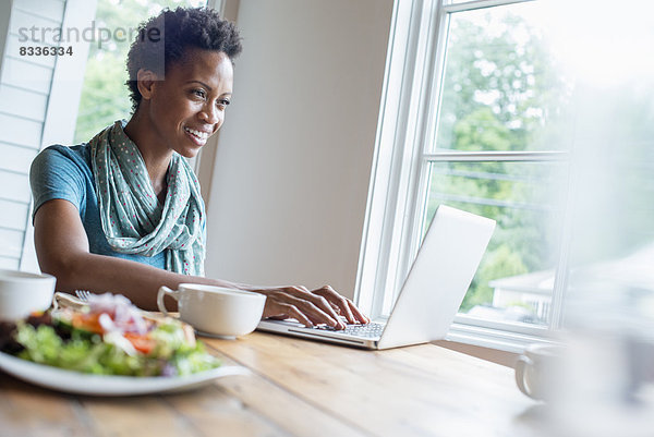 Eine Frau sitzt in einem Café mit einer Tasse Kaffee und einer Mahlzeit. Sie benutzt einen Laptop.