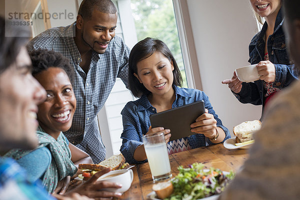 Eine Gruppe von Menschen  die sich in einem Café zu einer Mahlzeit trifft. Mit digitalen Tablets und Smartphones.