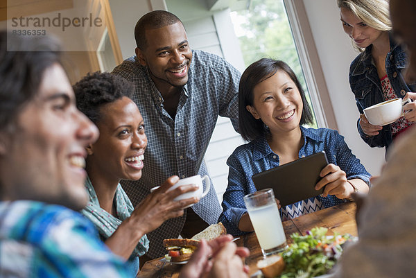 Eine Gruppe von Menschen  die sich in einem Cafe trifft. Mit digitalen Tablets und Smartphones.