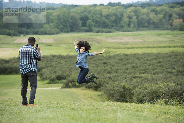 Ein Mann fotografiert eine Frau  die in die Luft springt und vor Freude mit ausgestreckten Armen springt.