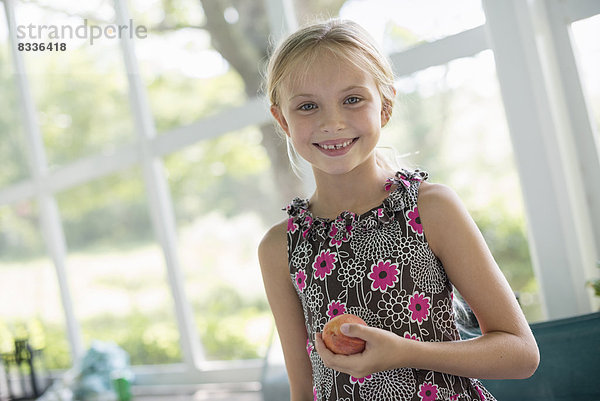 Ein junges Mädchen in einem Blumenkleid  das eine Pfirsichfrucht hält.