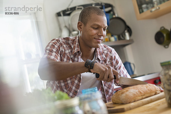 Ein Mann in einer Küche  der einen Laib Brot schneidet.
