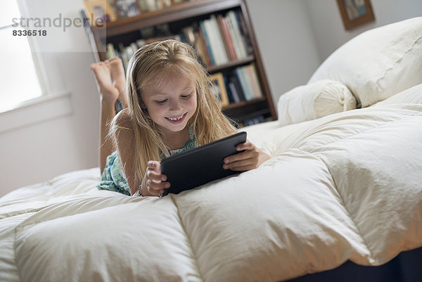 Ein junges Mädchen sitzt auf ihrem Bett und benutzt ein digitales Tablett.