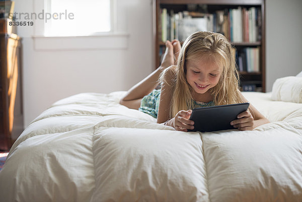 Ein junges Mädchen sitzt auf ihrem Bett und benutzt ein digitales Tablett.