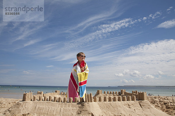 Ein Junge steht neben einer Sandburg  auf einem Sandhügel. Der Strand.
